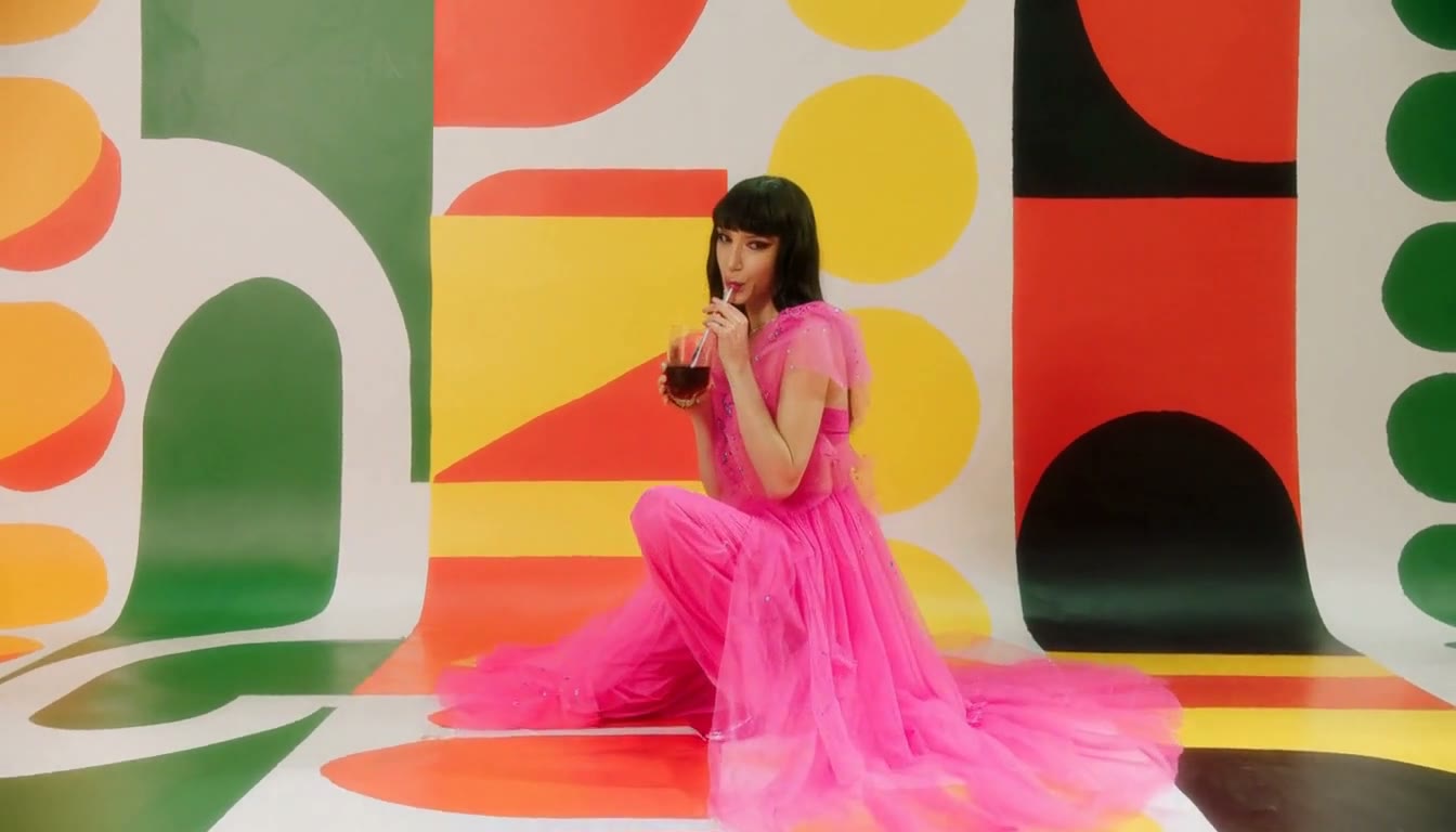 MiniMax H3 AI video example showing a stylish woman in a vibrant pink outfit sips a drink with a straw while squatting on a striped surface