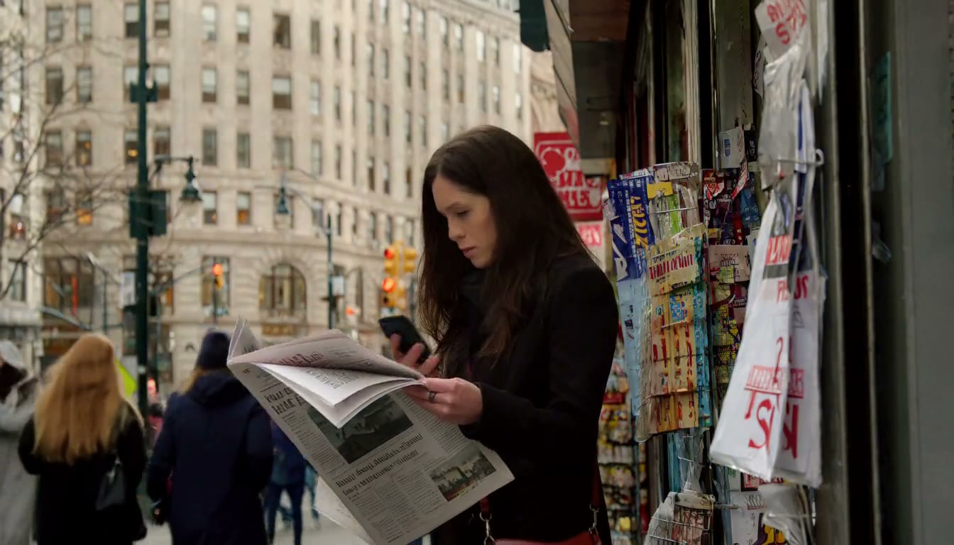 MiniMax H3 AI video example showing a woman stands by a newsstand, reading a newspaper and checking her phone
