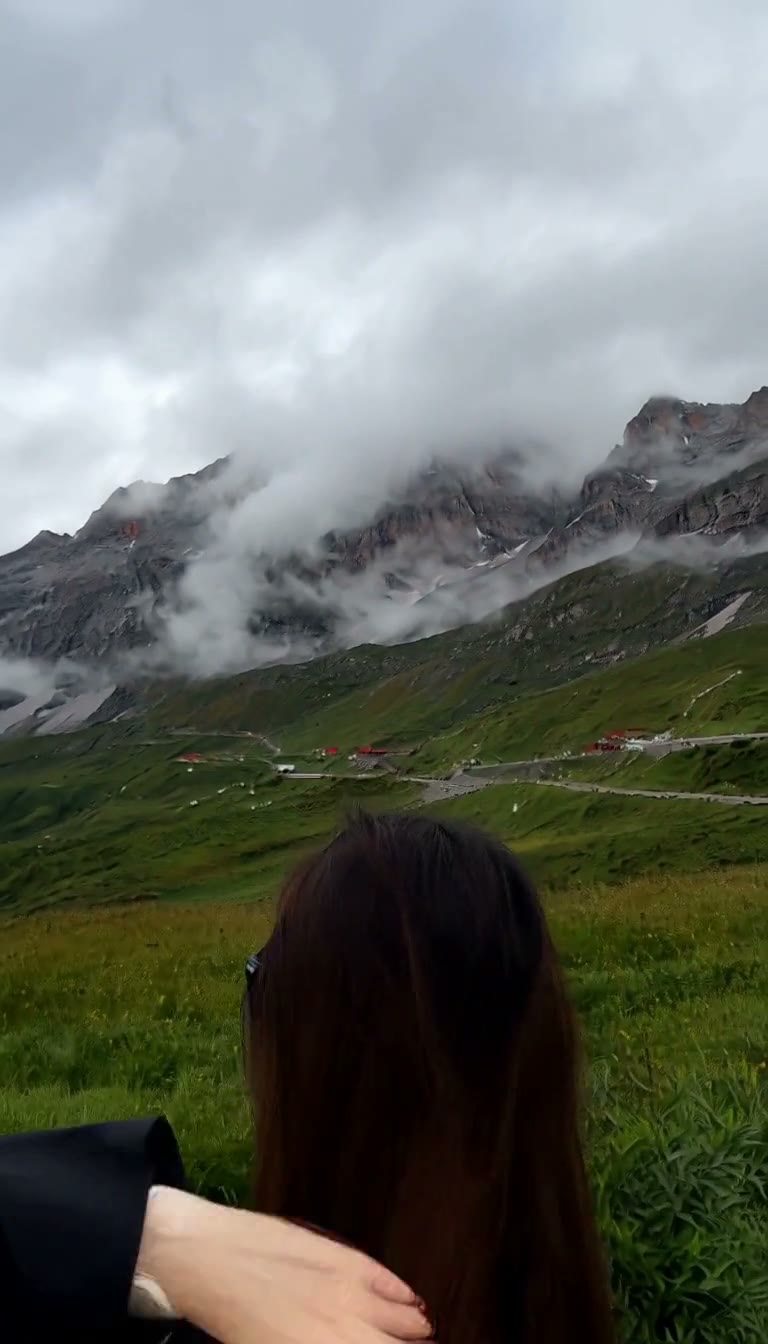 MiniMax H3 AI video example showing a person adjusts their hair in front of a mountainous backdrop and a city street setting